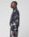 A person stands in profile wearing the LIVE FAST DIE YOUNG LFDY Performance Jacket with matching pants, featuring an allover print and reflective logo, set against a plain light gray background.