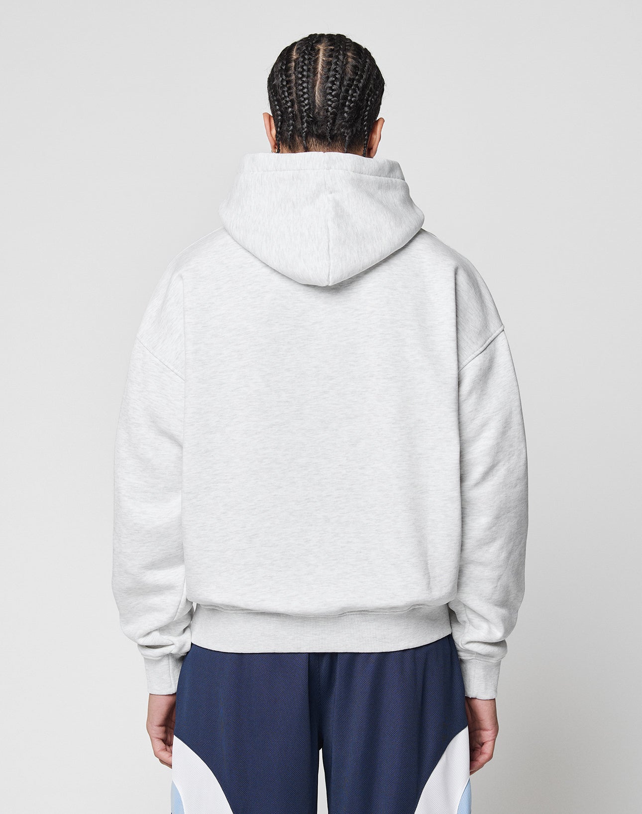 Person with braided hair, seen from behind, wearing the LIVE FAST DIE YOUNG Live Fast College Hooded in light gray and navy athletic pants with white and light blue accents, standing against a plain light background.