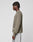 A person with short twisted hair stands sideways against a plain background, holding a phone and wearing the LIVE FAST DIE YOUNG LFDY Knit Sweater in olive green with light gray shorts.