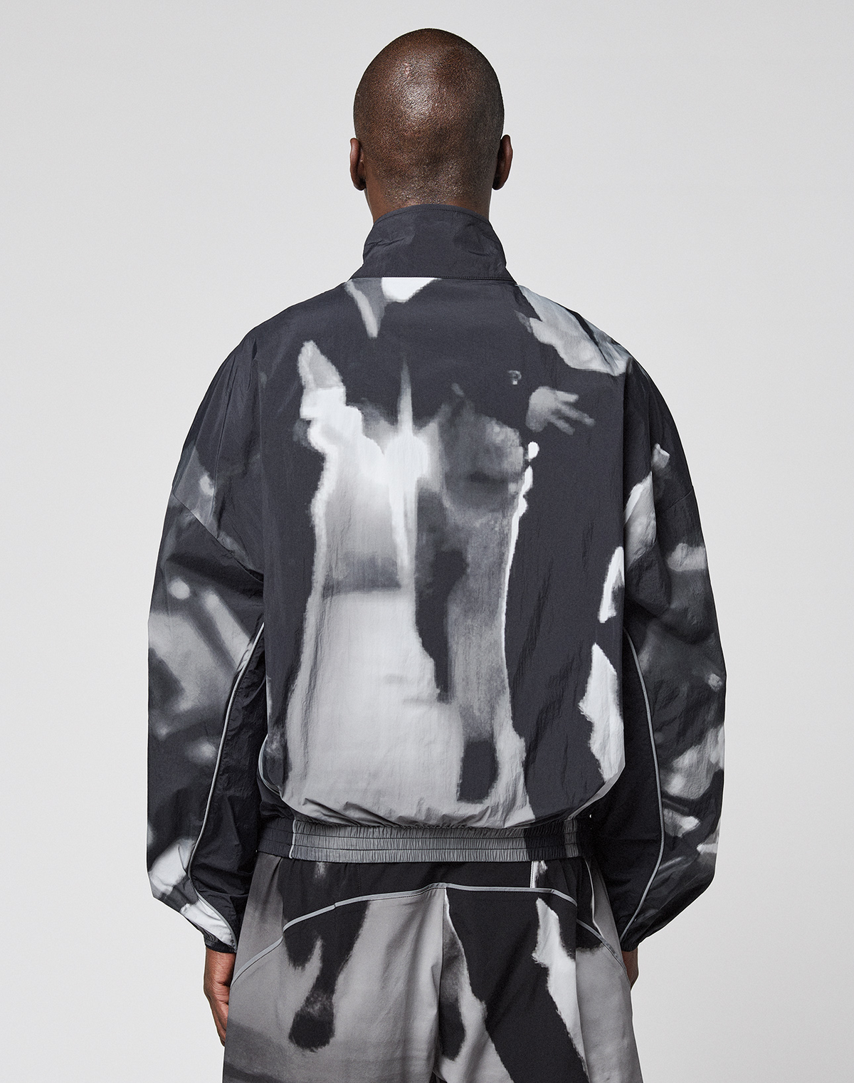 A person with closely shaved hair is seen from behind wearing a loose-fitting black and white LFDY Performance Jacket by LIVE FAST DIE YOUNG, along with matching pants featuring a reflective logo print, set against a plain gray background.