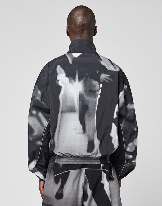 A person with closely shaved hair is seen from behind wearing a loose-fitting black and white LFDY Performance Jacket by LIVE FAST DIE YOUNG, along with matching pants featuring a reflective logo print, set against a plain gray background.