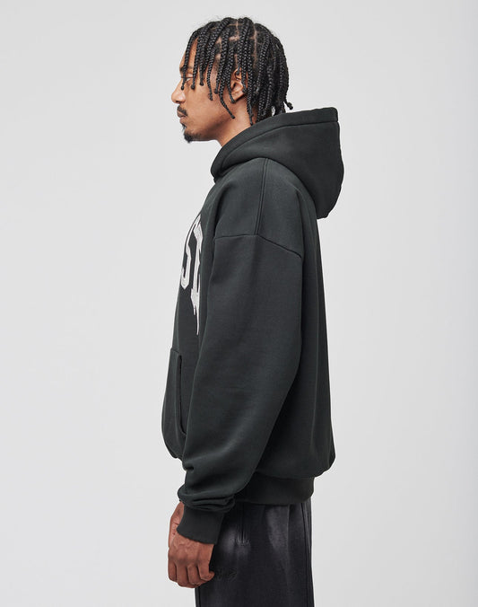 A man with braided hair stands in profile against a light gray background, wearing the LIVE FAST DIE YOUNG Live Fast Axe Hooded in black with white lettering and matching black pants.