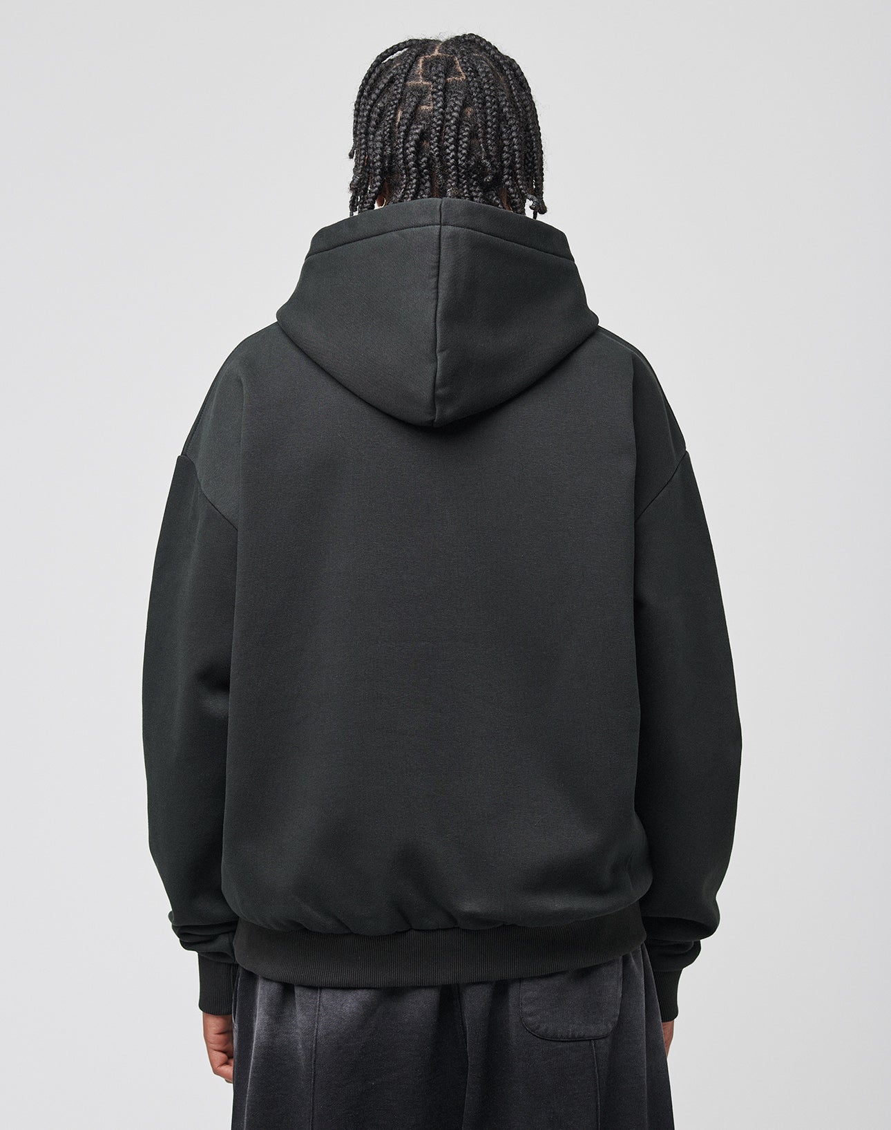 A person with braided hair, seen from behind, wears the LIVE FAST DIE YOUNG Live Fast Axe Hooded in oversize fit and dark pants, standing against a plain light gray background.