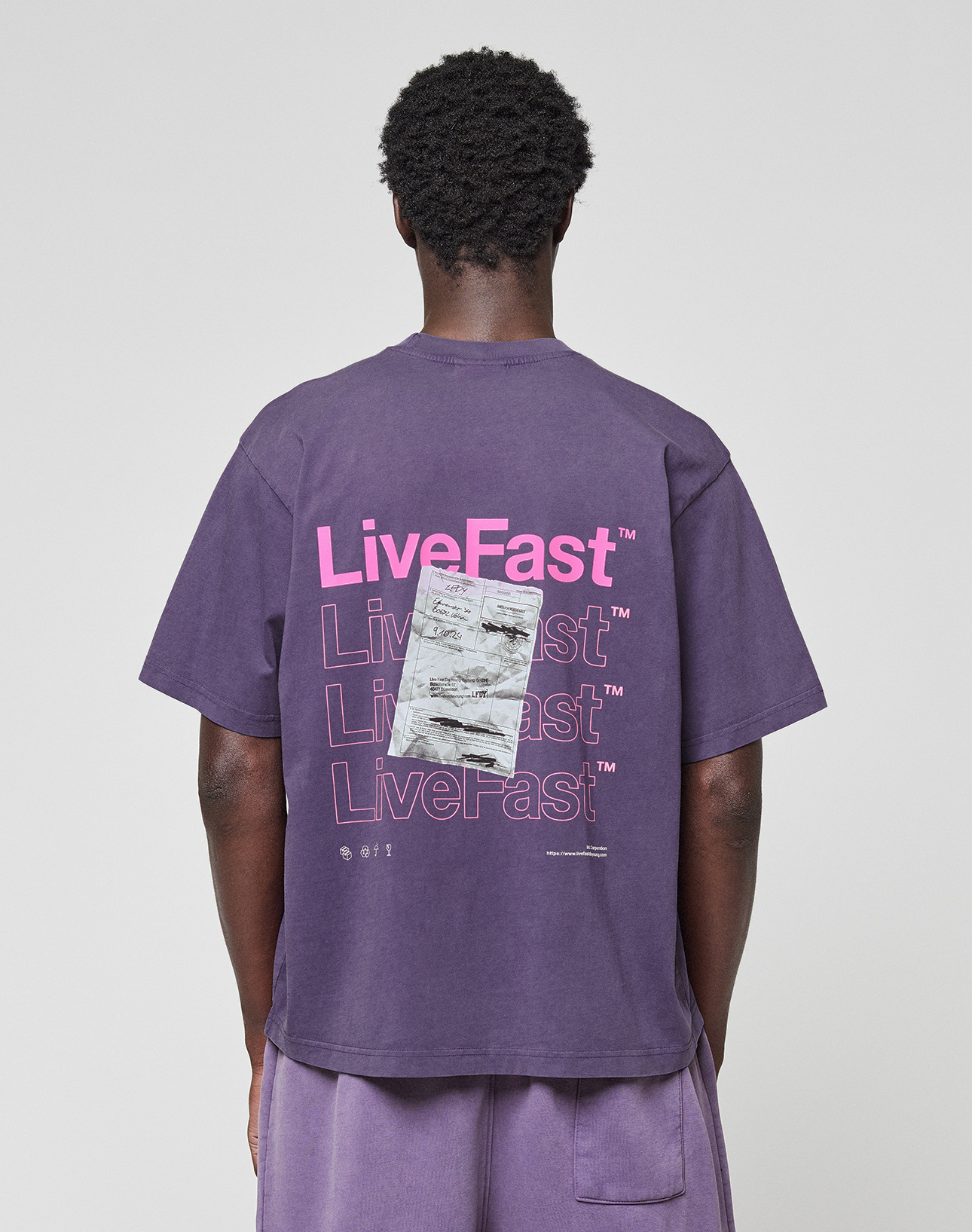 A person in a purple Basic Evidence Tee by LIVE FAST DIE YOUNG, made from 100% Baumwolle, featuring repeated “LiveFast” text and a graphic on the back. The front and back print design is shown from behind against a plain background. | model