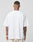 A person with tattoos on their head, neck, and arms is shown from behind wearing a LIVE FAST DIE YOUNG Basic Heavy Tee in white (100% Baumwolle, oversize fit), paired with light pants against a plain light gray background.