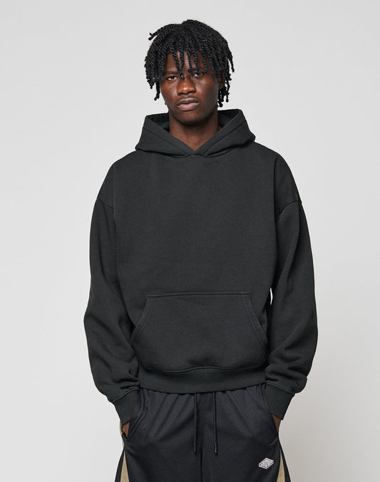 A young man with short, twisted hair wears a black LIVE FAST DIE YOUNG Basic Blank Hooded and black athletic pants, standing against a plain light gray background. He looks directly at the camera with a neutral expression.