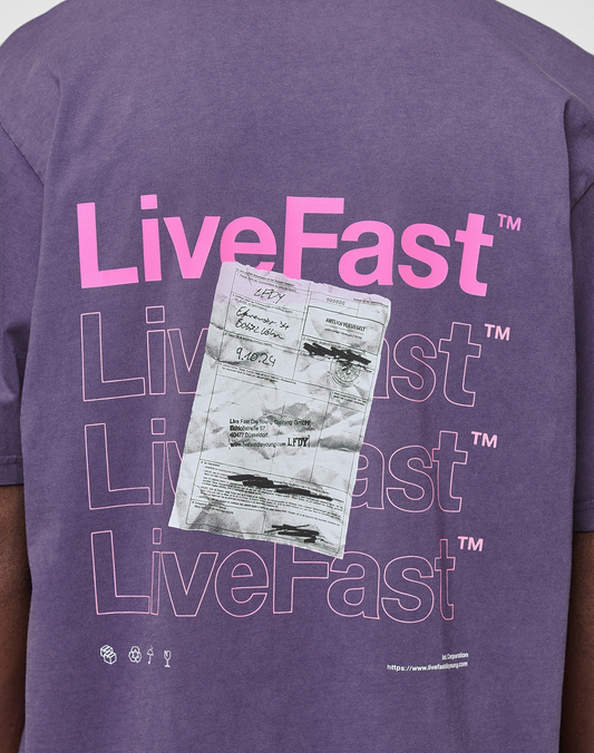 Wearing the Basic Evidence Tee by LIVE FAST DIE YOUNG: an oversize purple shirt featuring bold pink "LiveFast" front and back prints, a large crumpled paper graphic with handwritten notes, small logos, website, and 100% Baumwolle tag near the hem.