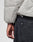 A close-up shows a person wearing the LIVE FAST DIE YOUNG Live Fast Puffer Jacket in light gray with dark gray jeans, highlighting part of their left arm and hand near the back pocket.