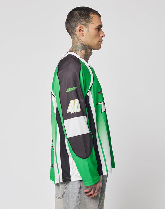 A man with short hair and neck tattoos stands in profile, wearing the LIVE FAST DIE YOUNG LFDY Motorcross Jersey—an oversize green, black, and white long-sleeve with multi-logo prints and 40 on the sleeve—paired with light-washed jeans.