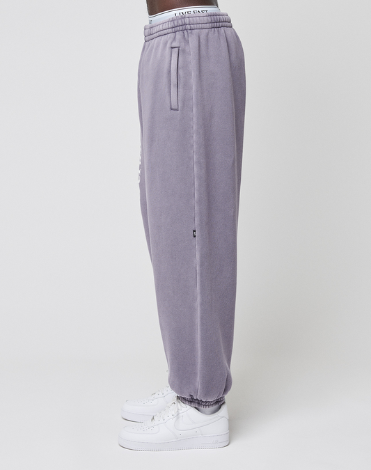 A person stands in profile wearing LIVE FAST DIE YOUNG's LFDY Hotline Loose Jogger in light purple with elastic waistband and cuffs, paired with white Nike sneakers, set against a plain white background.