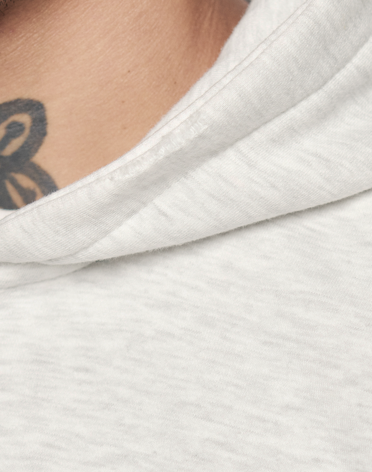 Close-up of a person in the LIVE FAST DIE YOUNG Basic Hooded Zip, Oversize Fit, light gray color, showing fabric texture, a glimpse of their neck, and part of a black tattoo.