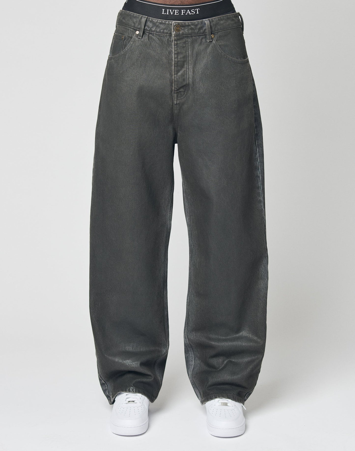 Someone stands against a plain white background wearing LIVE FAST DIE YOUNG’s LFDY Coated Baggy Denim in faded black, featuring 100% Baumwolle and gerades Bein, paired with white sneakers and black LIVE FAST waistband underwear.