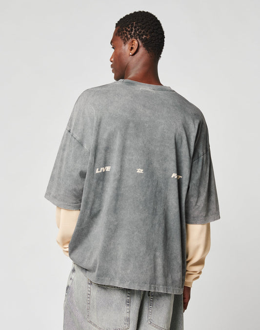 A person faces away, wearing a LIVE FAST DIE YOUNG LFDY Double Layered Longsleeve with small text and symbols on the back, styled in an oversize fit over light gray jeans against a plain light background.