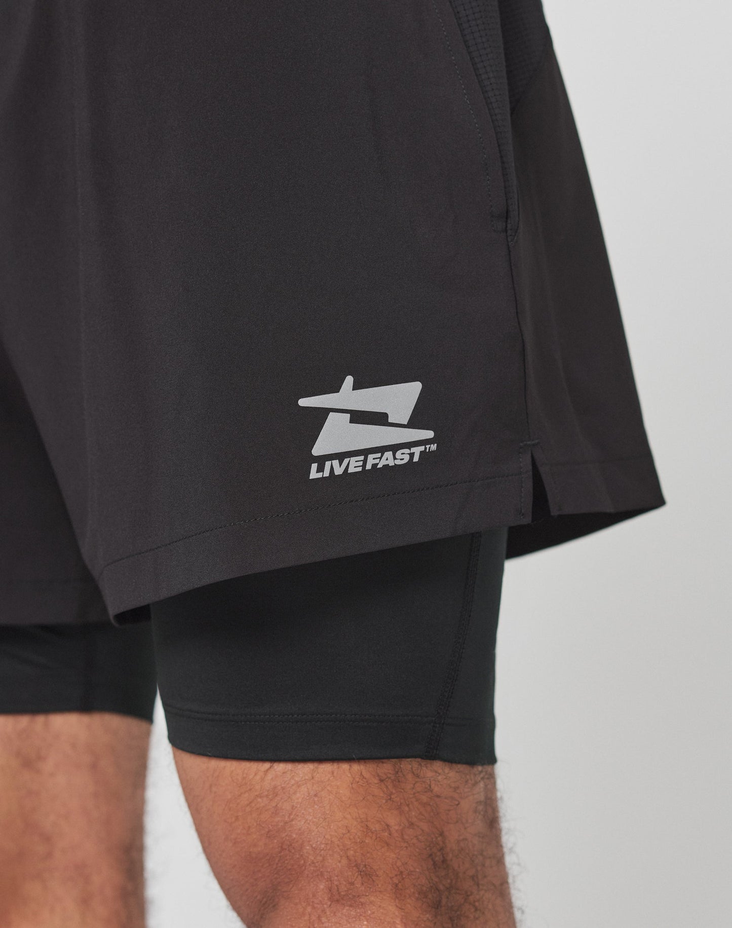 LIVE FAST DIE YOUNG Live Fast Performance Running Shorts feature an overlapping black design with “LIVE” on the left inner leg and “FAST” on the right in bold white. Regular fit, shown on a plain light background.