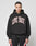 A person with braided hair models the LIVE FAST DIE YOUNG Live Fast College Hooded—an oversize black hoodie with a bold white and red front print, made from 65% Baumwolle, against a plain light background.