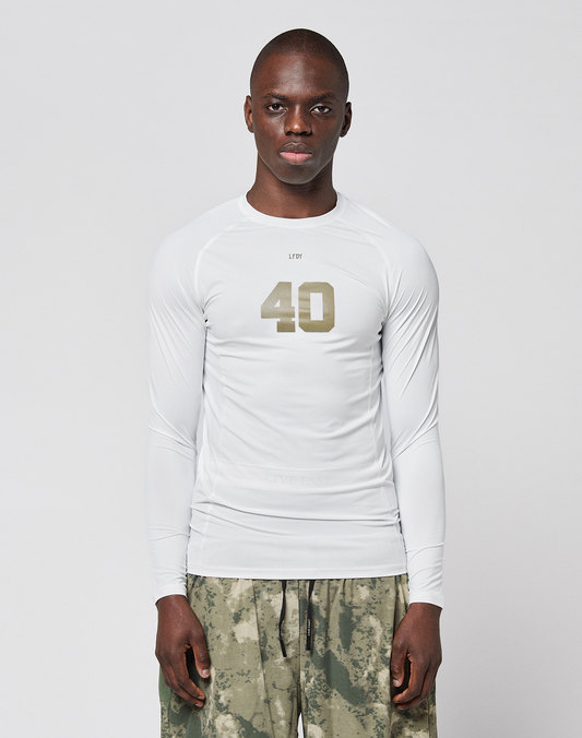 A person faces forward in a LIVE FAST DIE YOUNG LFDY Performance Slim Longsleeve, white with the number 40 on the front, and green-gray camouflage shorts made from leichtes Obermaterial, set against a plain light background. | model