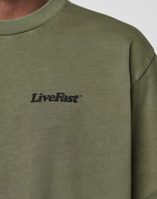 Close-up of a person wearing the Basic 210 Tee by LIVE FAST DIE YOUNG in olive green, featuring 'LiveFast™' in black on the upper left chest. The oversized fit and 100% cotton ensure comfort and style; only part of the neck and shoulder are visible.