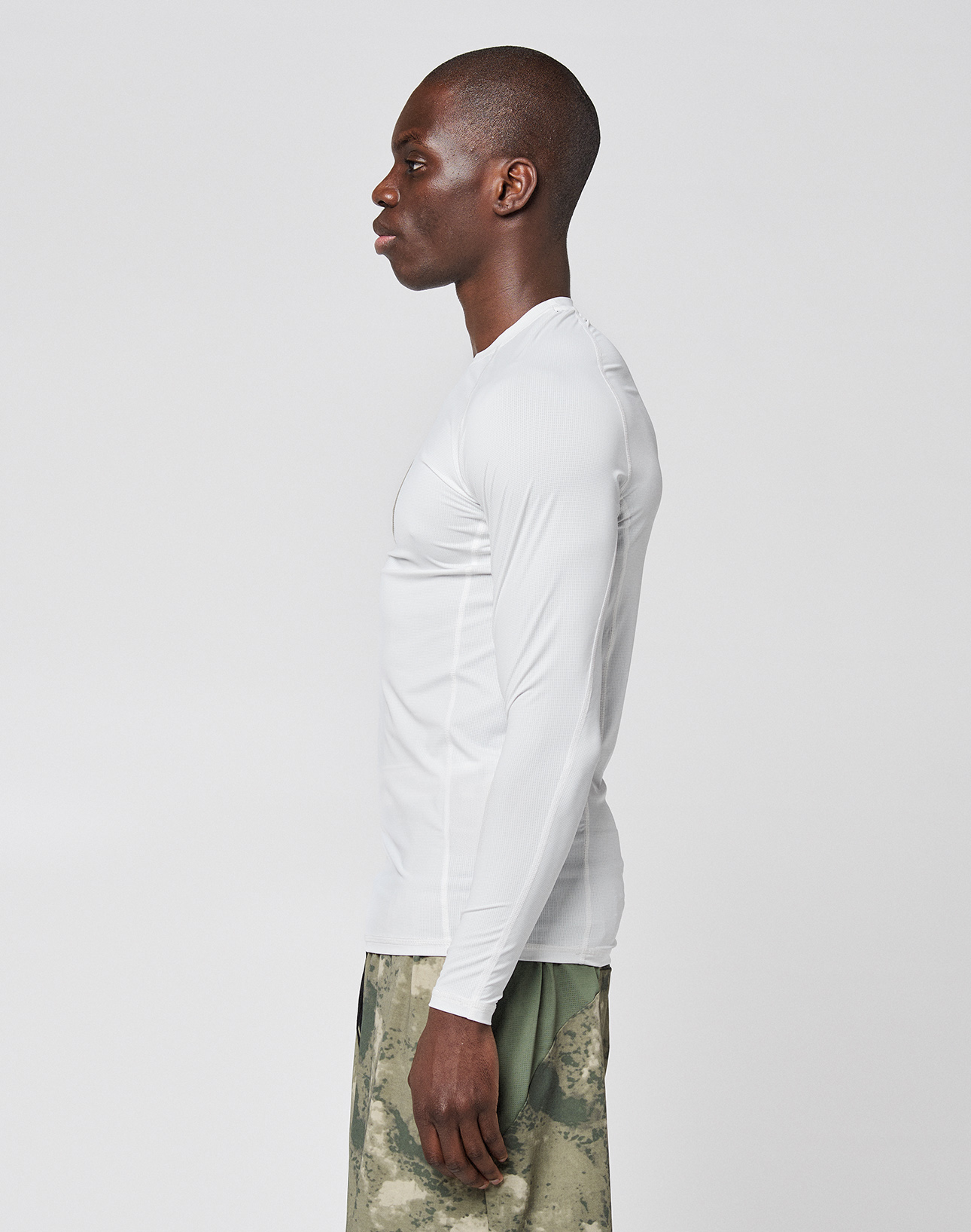 A man stands in profile against a plain background, wearing a LIVE FAST DIE YOUNG LFDY Performance Slim Longsleeve in white and green camouflage shorts made from lightweight material.