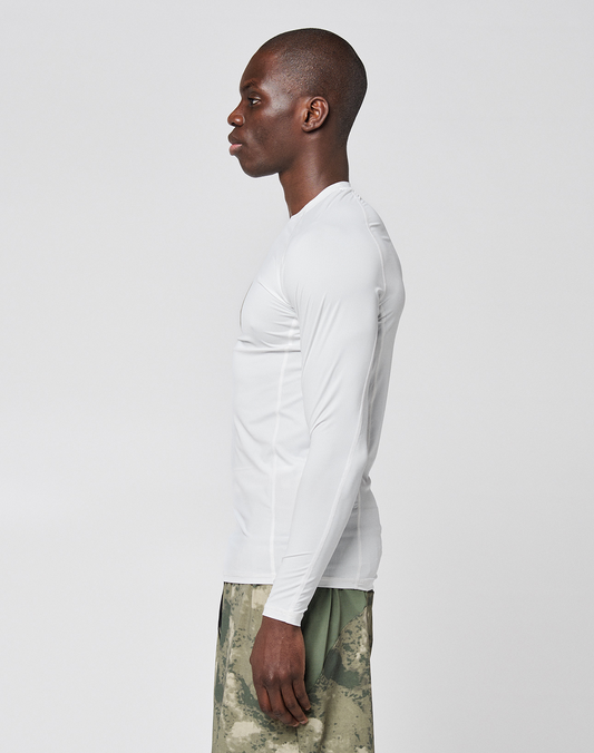 A man stands in profile against a plain background, wearing a LIVE FAST DIE YOUNG LFDY Performance Slim Longsleeve in white and green camouflage shorts made from lightweight material.