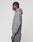 A person with braided hair stands sideways, wearing the LIVE FAST DIE YOUNG Basic +49 Hooded oversized grey sweatshirt with front print and matching cotton sweatpants against a plain light background.