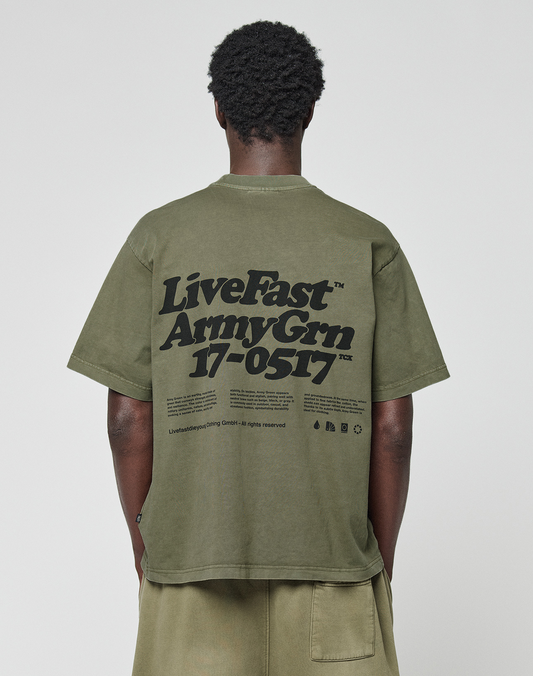 A person faces away, wearing a LIVE FAST DIE YOUNG Basic 210 Tee in olive green (100% Baumwolle) with bold black "LiveFast ArmyGrn 17-0517" front and back prints, small lower back text, and matching shorts. | model