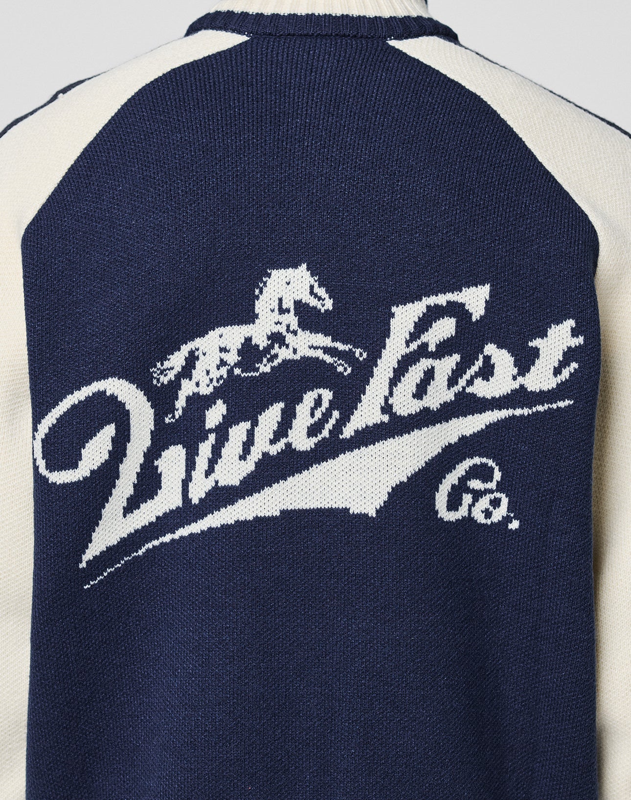 Navy blue and white Boxy Knit Zip Jacket by LIVE FAST DIE YOUNG, featuring raglan sleeves and a horse and rider graphic above stylized "Live Fast Co." logo detail on the back.
