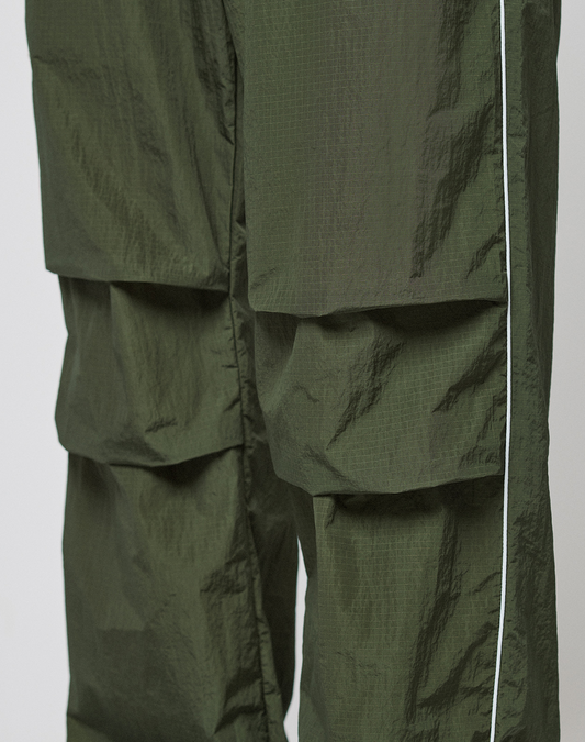Close-up of LIVE FAST DIE YOUNG LFDY Nylon Trackpants in olive green, featuring a wide fit, large pockets, a white side stripe, and a slightly crinkled polyamide texture.