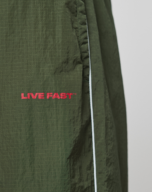 Close-up of LFDY Nylon Trackpants by LIVE FAST DIE YOUNG: dark green, wide fit with a white side stripe and red LIVE FAST logo embroidered on the pocket.