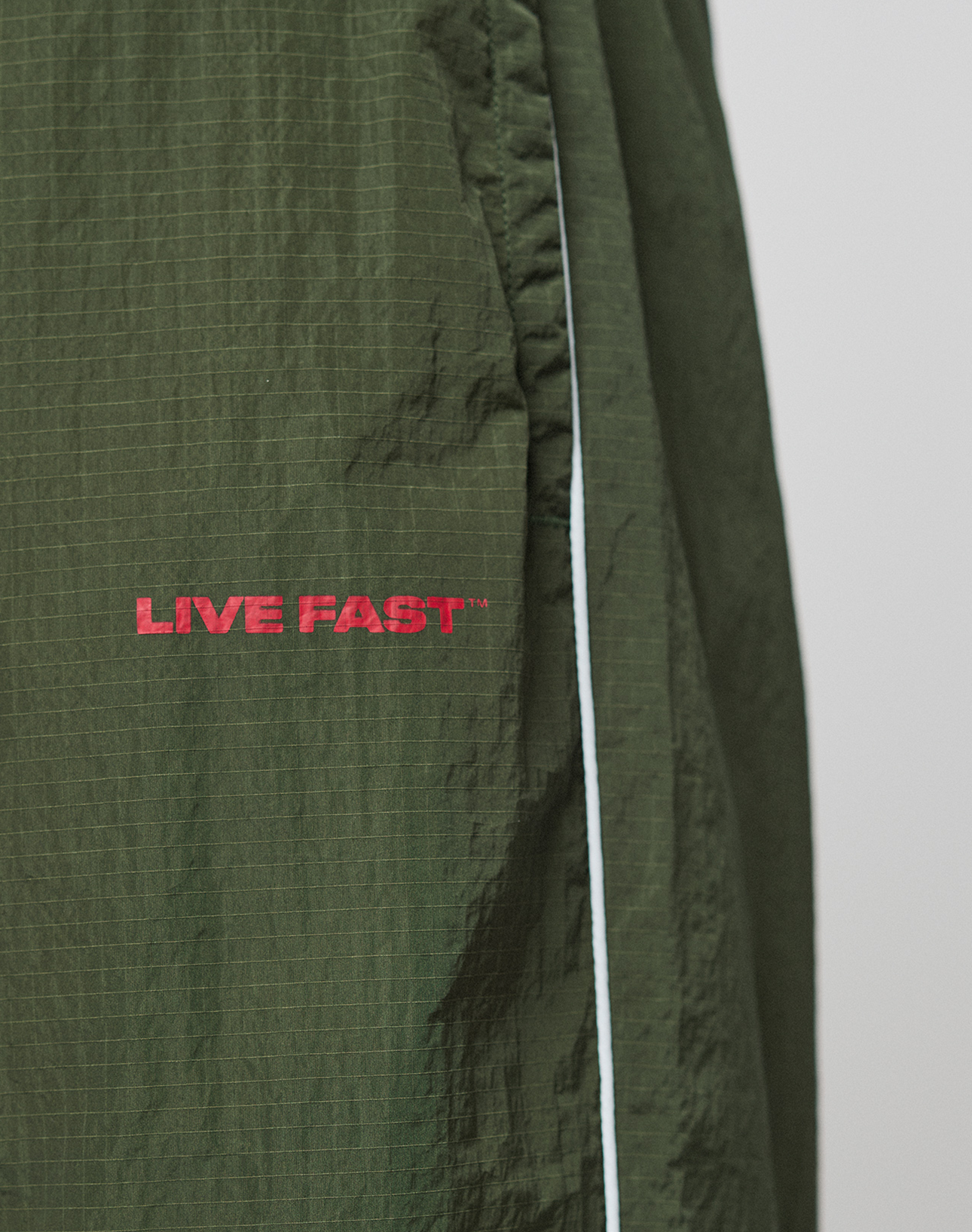 Close-up of LFDY Nylon Trackpants by LIVE FAST DIE YOUNG: dark green, wide fit with a white side stripe and red LIVE FAST logo embroidered on the pocket.