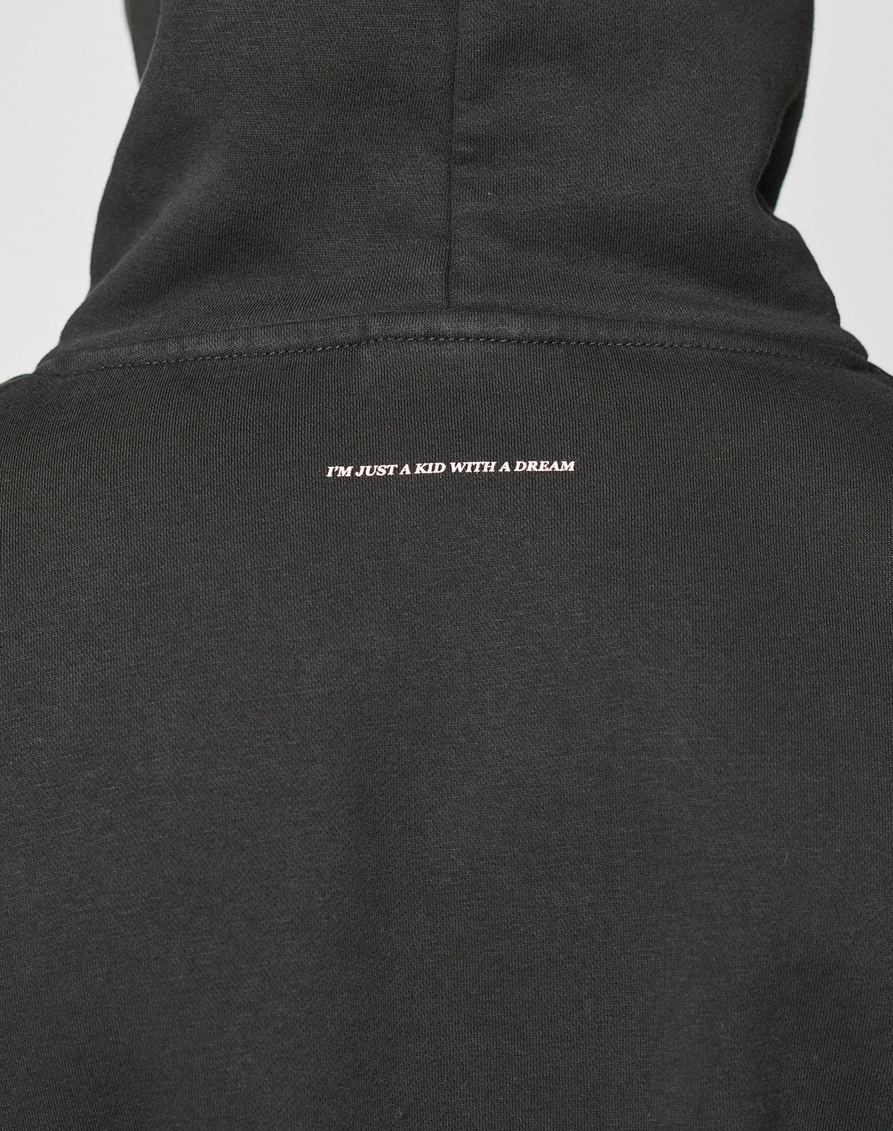 A close-up of the Live Fast College Hooded by LIVE FAST DIE YOUNG in black, made from 65% Baumwolle in an oversize fit, featuring IM JUST A KID WITH A DREAM printed in small white letters below the hood.