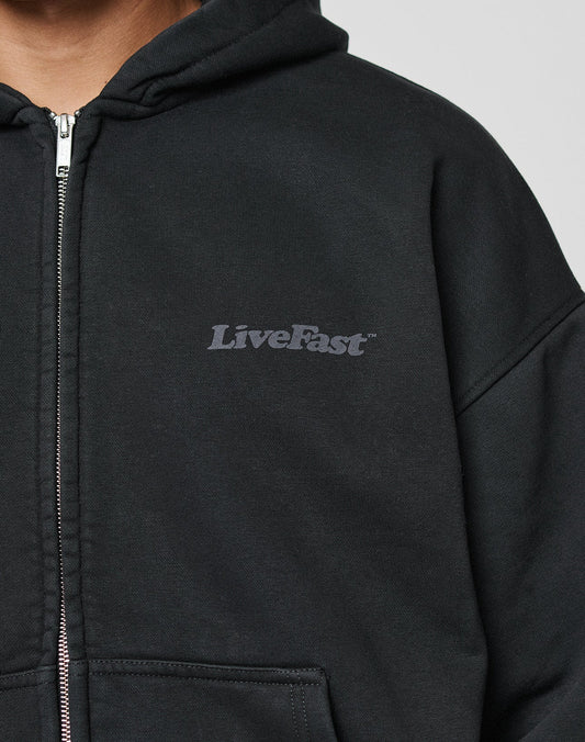 A person wears the LIVE FAST DIE YOUNG Basic 510 Hooded Zip, a black hoodie with LiveFast in gray on the left chest, made from durable 510 gsm fabric. Only their upper torso is shown against a plain background.