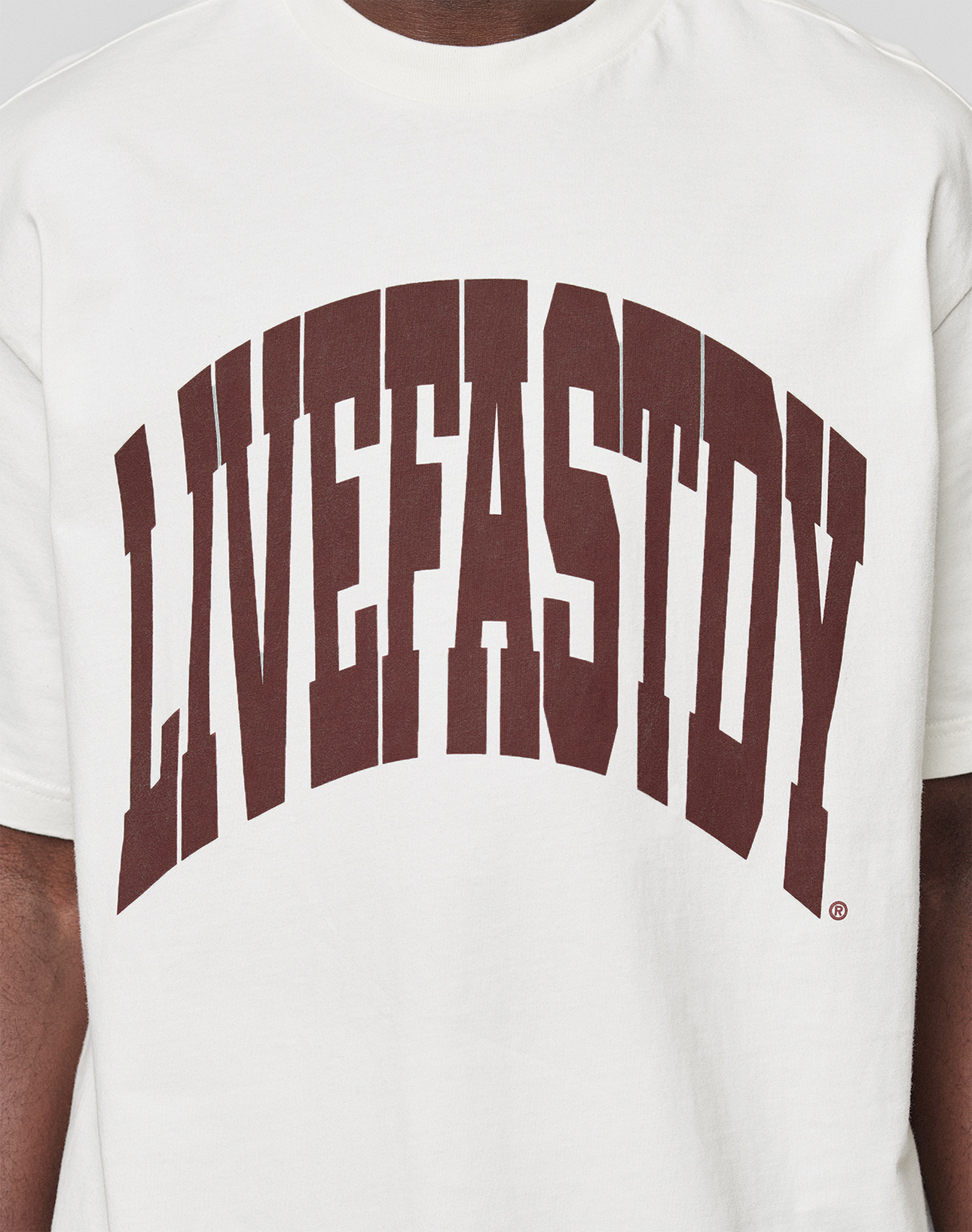 A person wears the LFDY Block Tee by LIVE FAST DIE YOUNG—an oversized white T-shirt featuring a bold, dark brown "LIVEFASTDY" arched front print. Made from 100% Baumwolle for comfort and style.