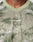 A close-up of a person wearing the LIVE FAST DIE YOUNG Camo Mesh Jersey, a light green camouflage-patterned shirt made from 100% polyester with LIVE FAST in reflective print on the chest. Only neck and upper chest are visible.