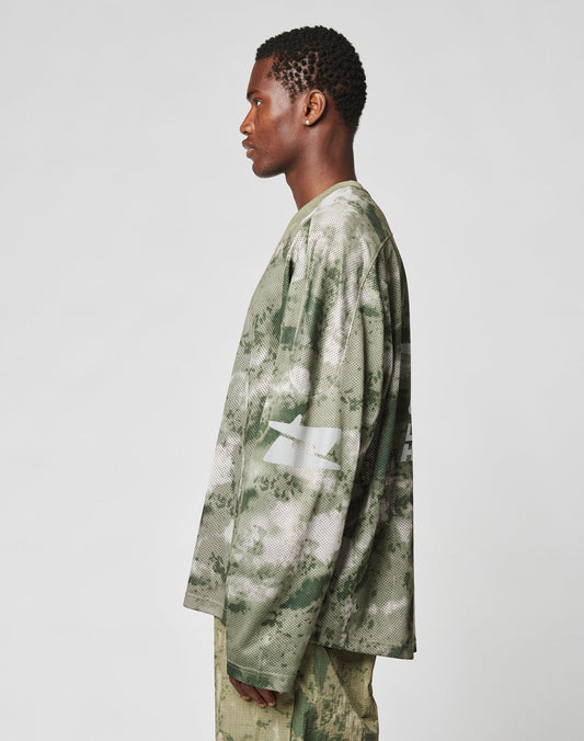 A man in profile wears the LIVE FAST DIE YOUNG Camo Mesh Jersey, an oversized long-sleeve shirt and pants set with a green and beige camo print made from 100% polyester, shown against a plain white background.