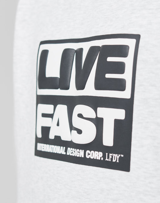 A close-up of the gray Live Fast Box Hooded by LIVE FAST DIE YOUNG, featuring an oversized fit and a black and white LIVE FAST puffer print, with INTERNATIONAL DESIGN CORP. LFDY™ below and a subtle flag-label detail.