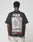 A person is seen from behind wearing the LIVE FAST DIE YOUNG LFDY F*ck Phones Tee, an oversized black cotton shirt with FUCK PHONES and Live Fast Archive plus a bag of old phones graphic on the back. Care instructions are on the label.