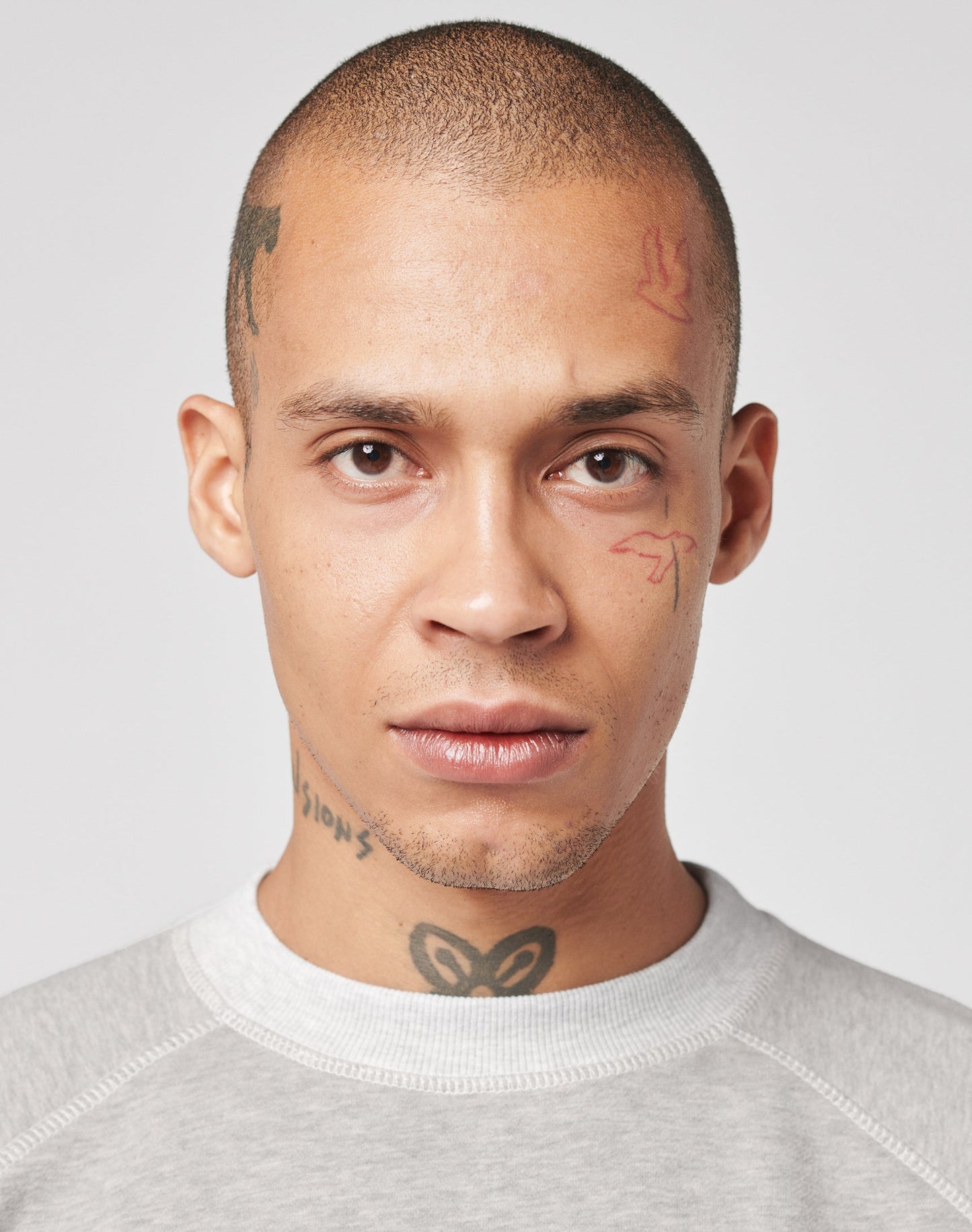 A person with a shaved head and visible face and neck tattoos wears the LFDY Script Sweater by LIVE FAST DIE YOUNG, featuring raglan sleeves and an oversize fit, looking directly at the camera against a light plain background.
