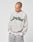 A person wears the LIVE FAST DIE YOUNG LFDY Script Sweater, a light gray oversized sweatshirt with raglan sleeves and Live Fast in dark green script on the front, looking down with hands in jean pockets against a plain background.