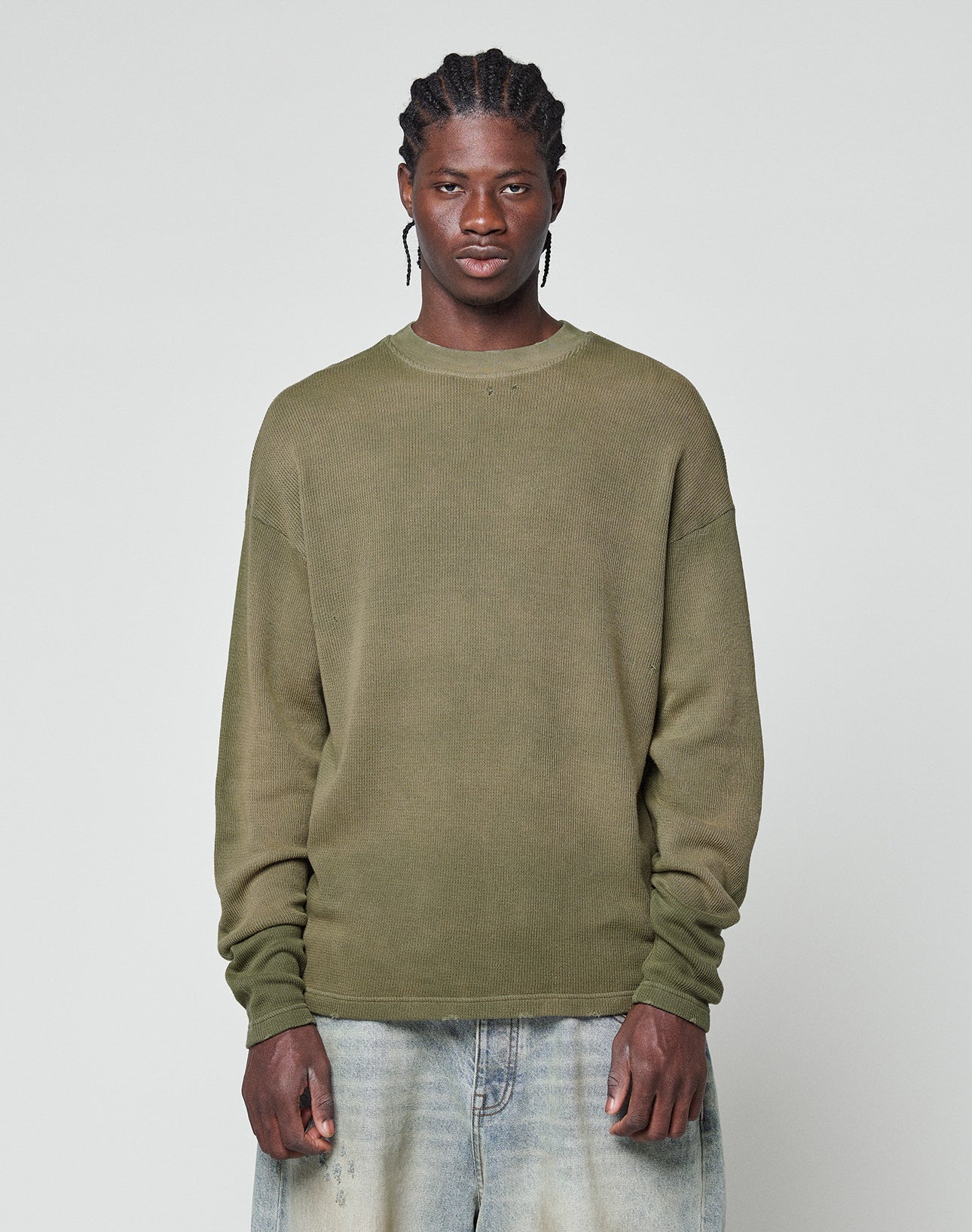 A person stands facing forward, wearing the olive LFDY Rib Knit Longsleeve by LIVE FAST DIE YOUNG and light blue jeans with a unique wash effect, set against a plain light gray background. | model