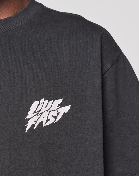 Close-up of a person wearing the LFDY Logo Tee by LIVE FAST DIE YOUNG, a dark gray 100% Baumwolle T-shirt featuring "LIVE FAST" in bold white letters as a front print on the left chest.