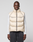 A man faces forward against a light gray background, wearing the LIVE FAST DIE YOUNG Live Fast Puffer Vest in light beige over a white long-sleeve shirt and dark drawstring pants.