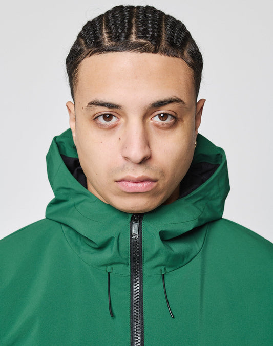 A person with braided hair wears the LIVE FAST DIE YOUNG Basic Shell Jacket with a water-repellent zipper and oversize fit, hood up, looking at the camera against a plain light background.