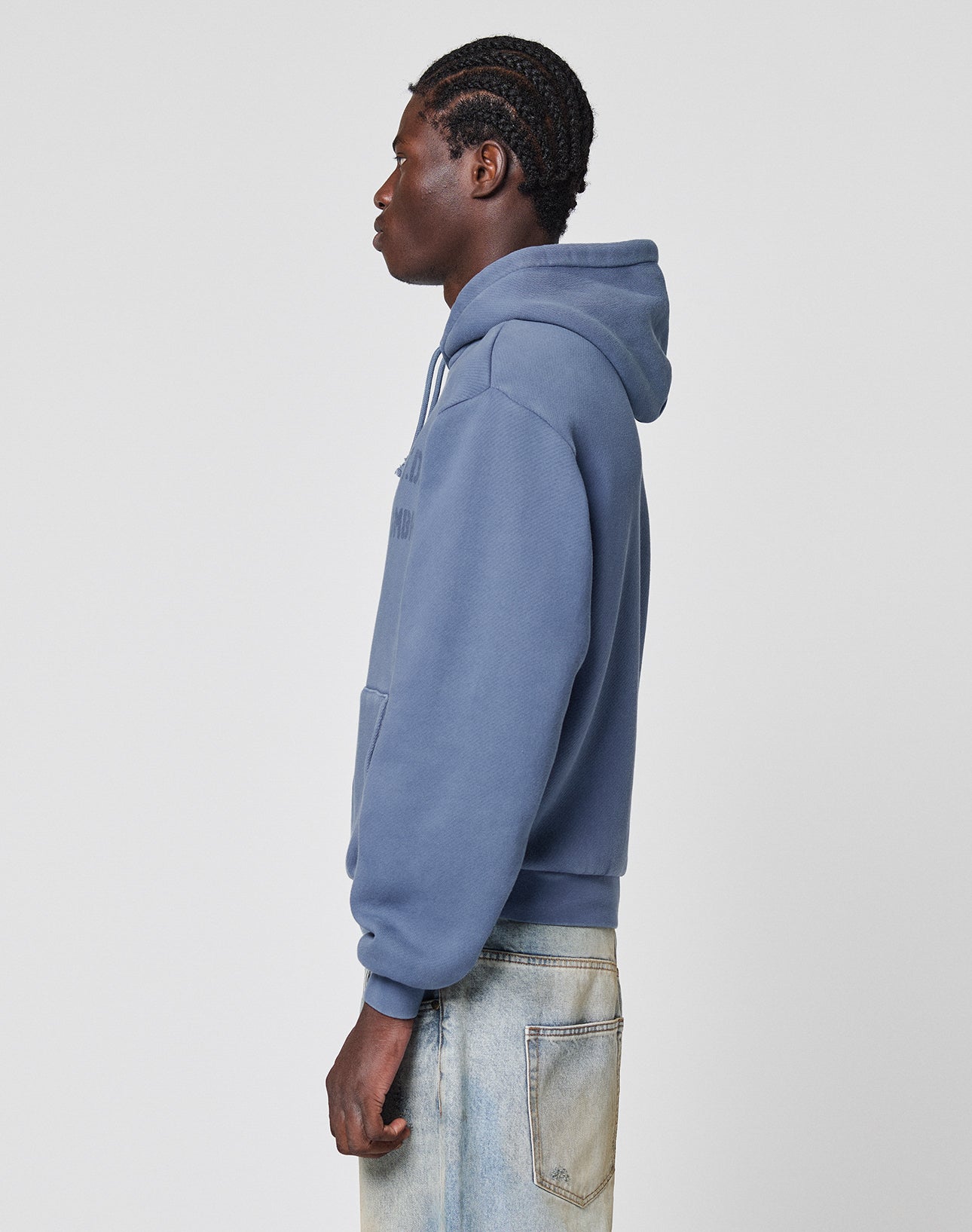 A person in profile wears the LFDY GmbH Hooded by LIVE FAST DIE YOUNG—an oversized blue hoodie with Kapuze mit Kordeln, vintage Waschung, front pocket, and hood down—styled with light blue jeans against a plain background.