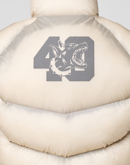 The back of the light beige Live Fast Puffer Vest by LIVE FAST DIE YOUNG has an oversized fit and a large dark gray “49” graphic with a snarling dog’s head in a spiked collar, printed over the transparent outer layer.