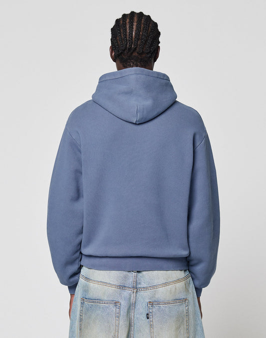 A person with braided hair is seen from the back wearing a blue LIVE FAST DIE YOUNG LFDY GmbH Hooded and light-washed jeans against a plain, light background.