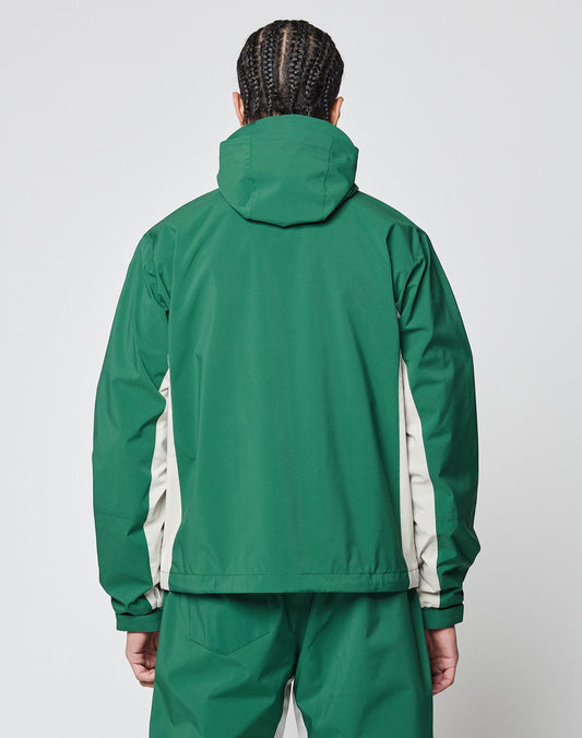 A person with braided hair, seen from the back, wears the LIVE FAST DIE YOUNG Basic Shell Jacket—a green hoodie with off-white side panels—and matching green pants with reflective print, standing against a plain light background.