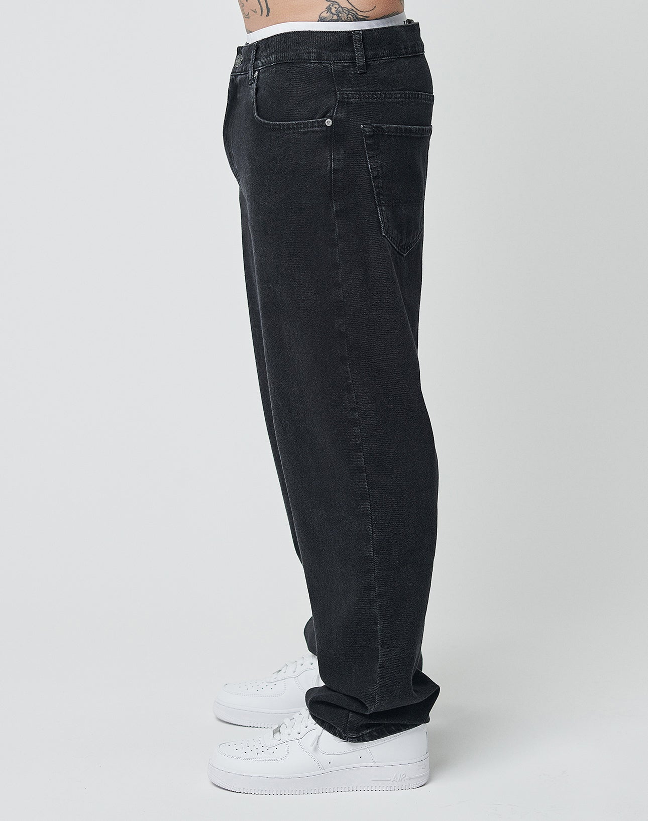 Eine Person trägt eine Wide Denim von LIVE FAST DIE YOUNG in Schwarz und weiße Sneaker, steht seitlich, sichtbar sind nur Unterkörper und Beine vor einem schlichten, hellen Hintergrund.