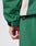 Close-up of a hand resting by the side, wearing LIVE FAST DIE YOUNG’s Basic Shell Jacket in an oversize green fit with black sleeve strap, light gray seam accent, and matching green pants.