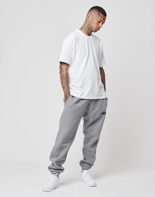 A man wearing the LIVE FAST DIE YOUNG LFDY Blank Tee stands against a plain white background in gray sweatpants and white sneakers, hands in pockets, looking down with a relaxed posture.