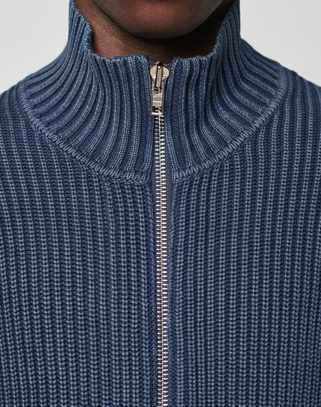Close-up of a person wearing the LFDY Knit Jacket by LIVE FAST DIE YOUNG, featuring a blue ribbed knit, Stehkragen, and silver zipper. The Regular Fit offers comfort; only the lower face and neck are visible.